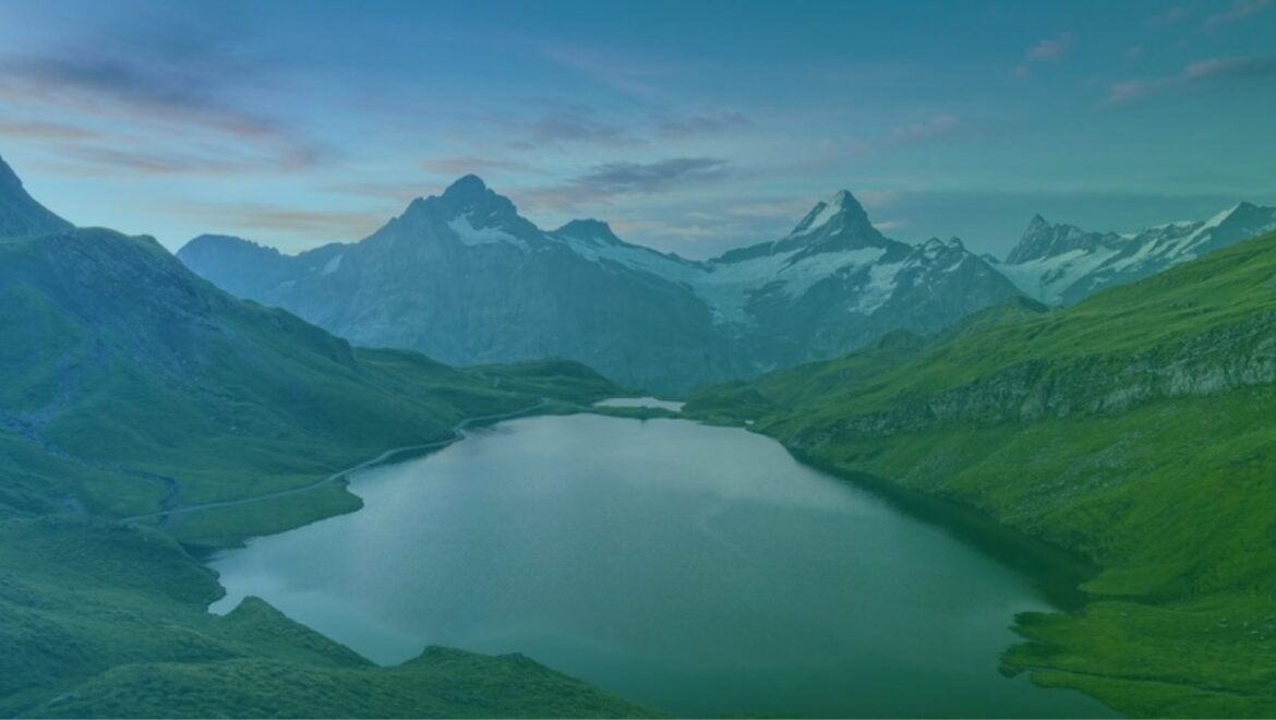 Alpine lake between green slopes with snow capped peaks in the distance